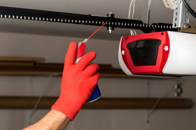 Technician performing a garage door opener repair, lubricating the opener chain mechanism to ensure smooth and quiet operation.